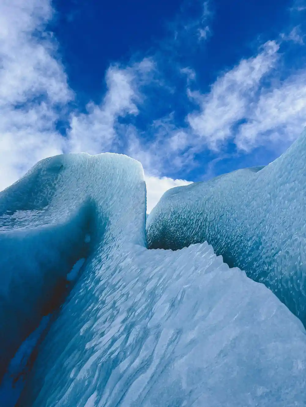 Blue ice formations against sky with white clouds