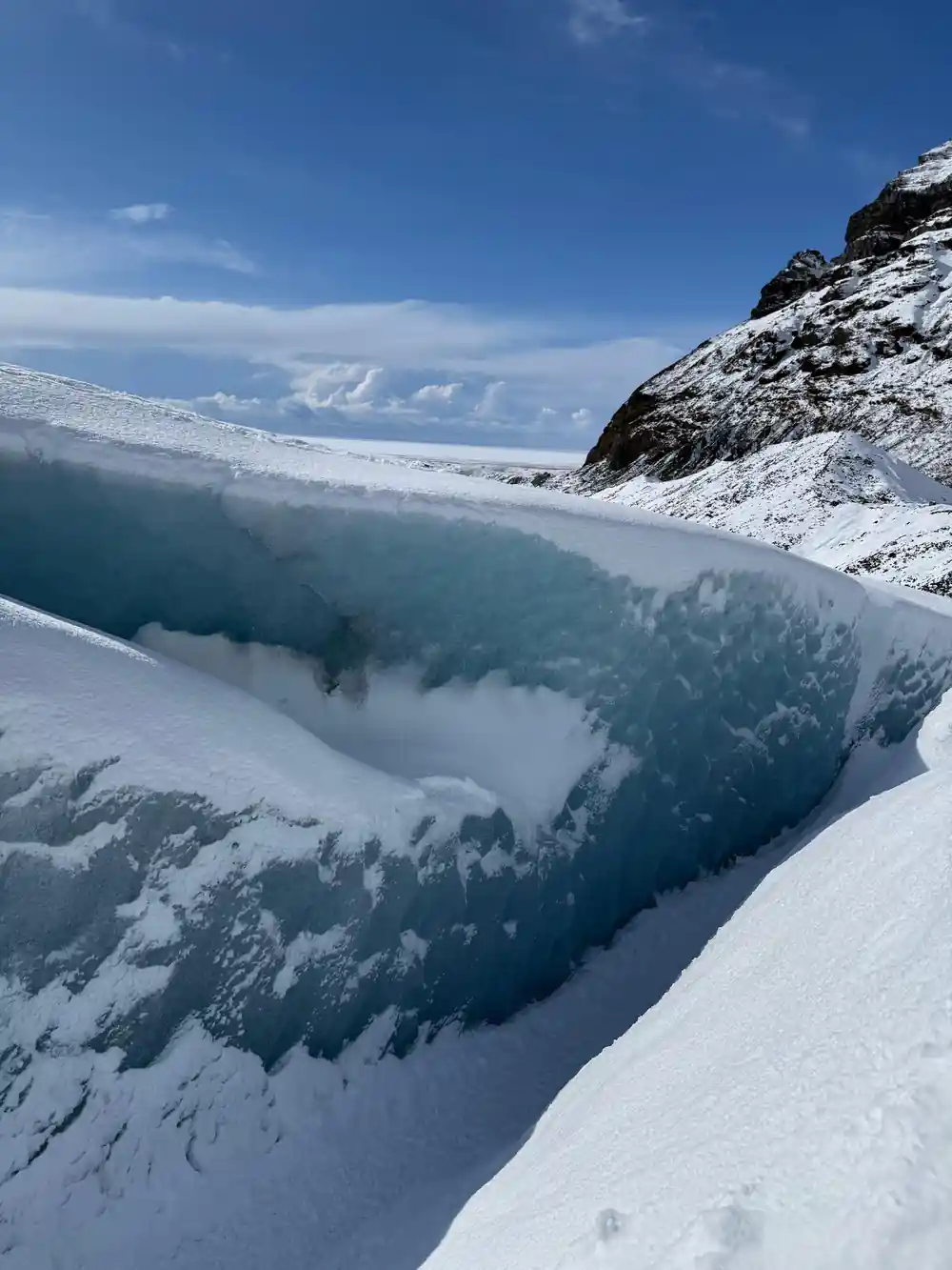 Deep glacier crevasse with forested valley below