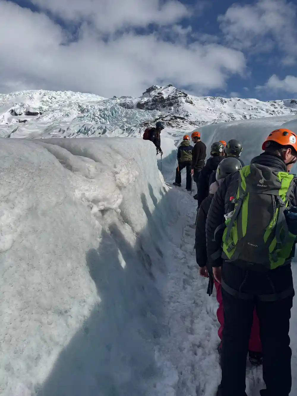 Group of hikers walking along narrow ice crevasse on glacier