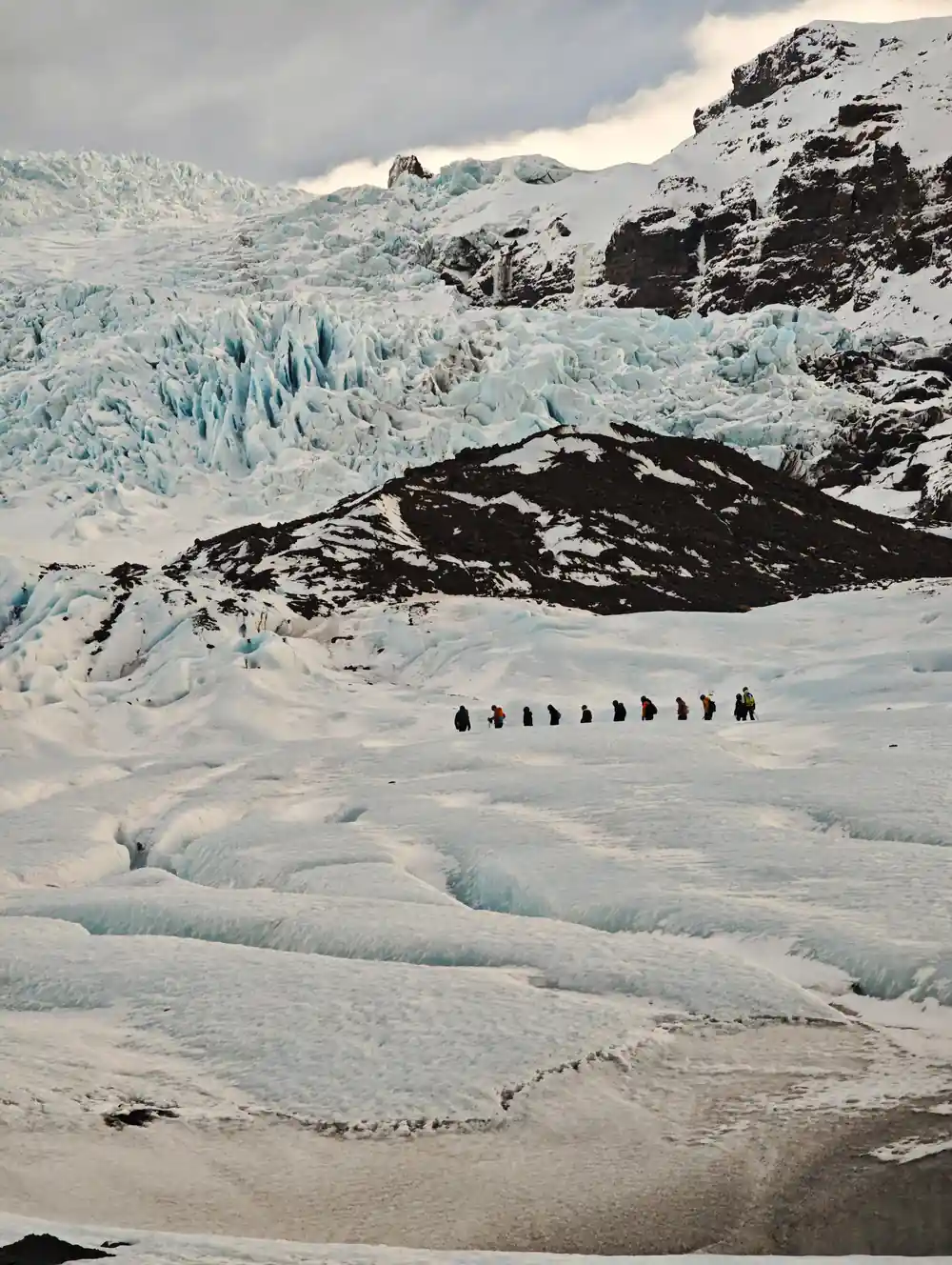 Group of hikers walking on glacier with icefall behind
