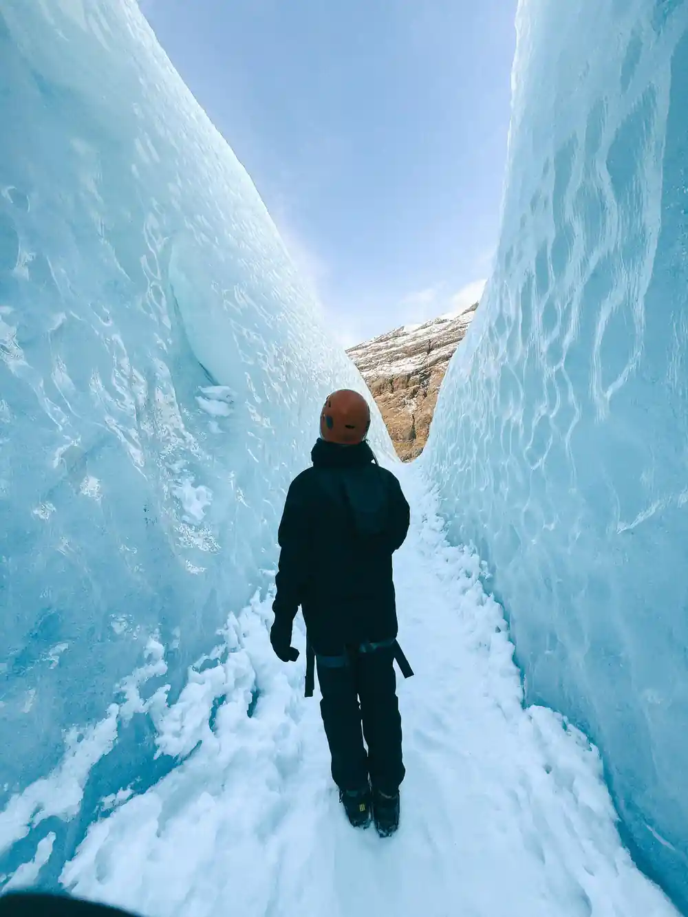 Hiker standing in tall ice canyon looking toward light
