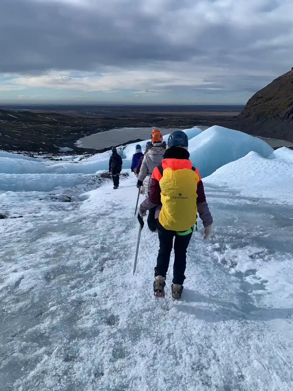 Hikers ascending icy slope with distant coastal landscape below