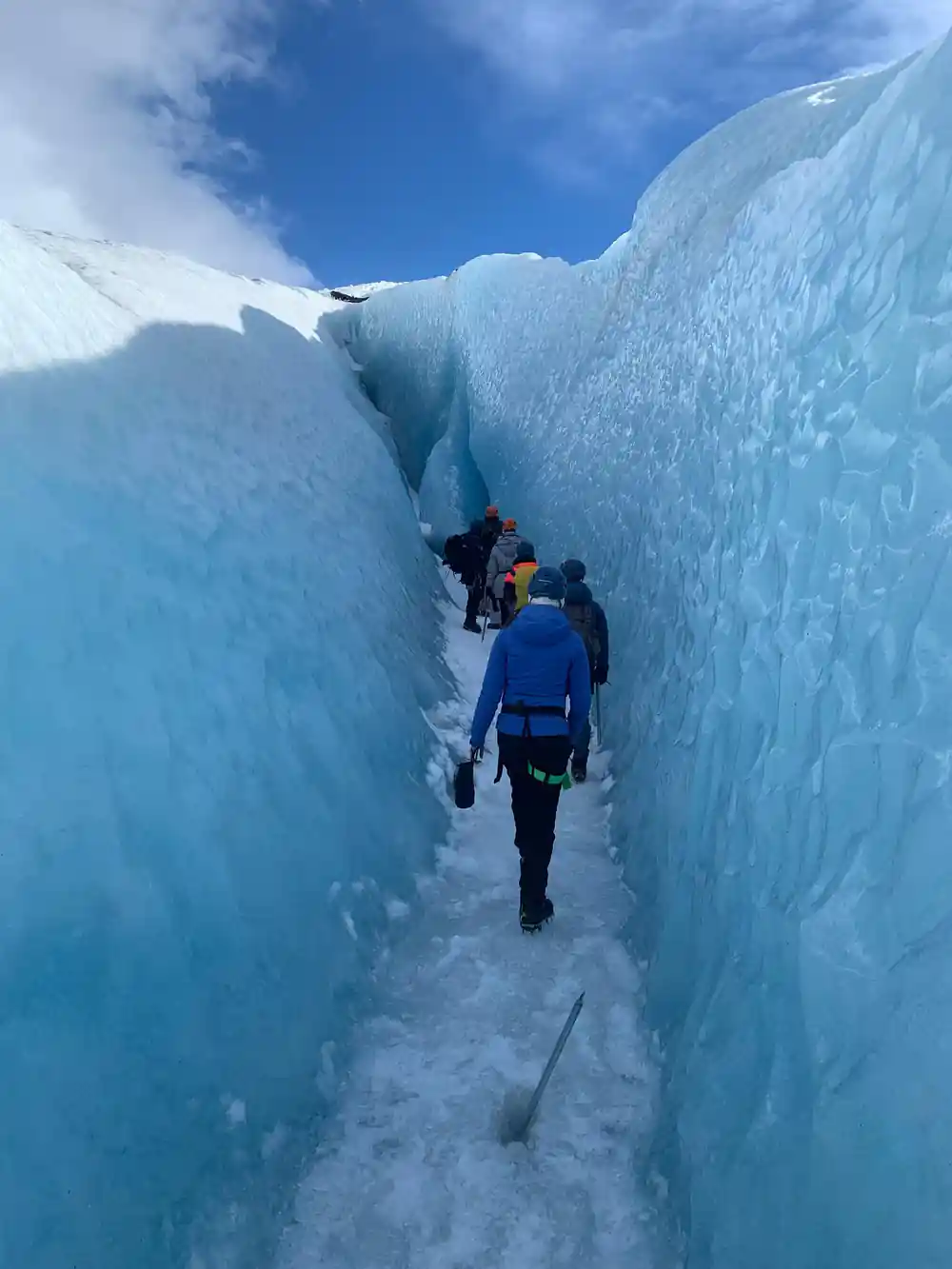 Hikers walking through narrow crevasse between tall blue ice walls