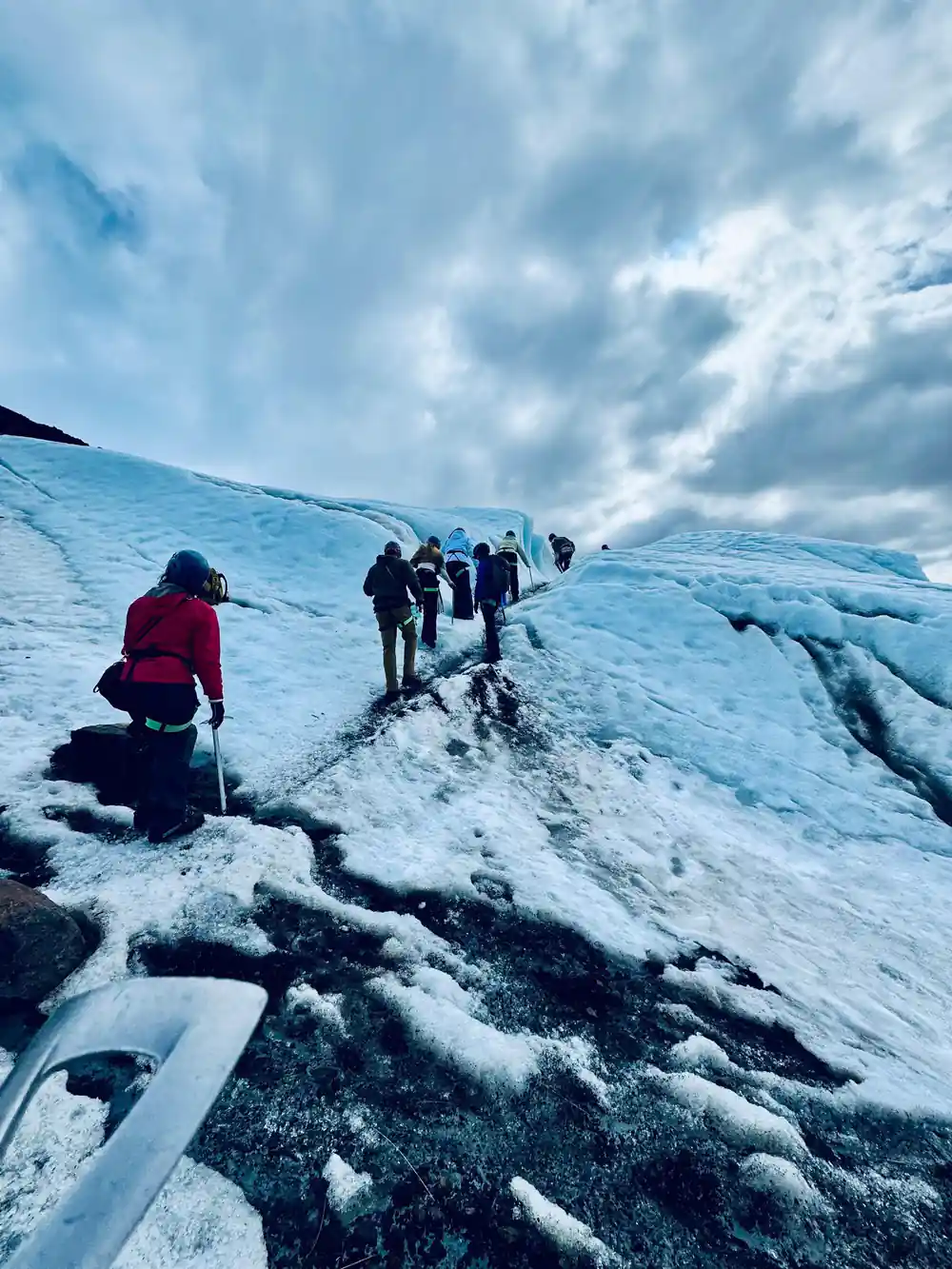 Line of hikers traversing across large glacier with mountains