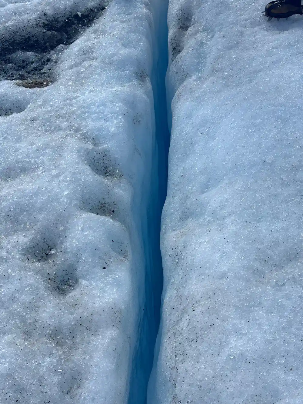 Narrow blue crevasse through white glacier ice close-up