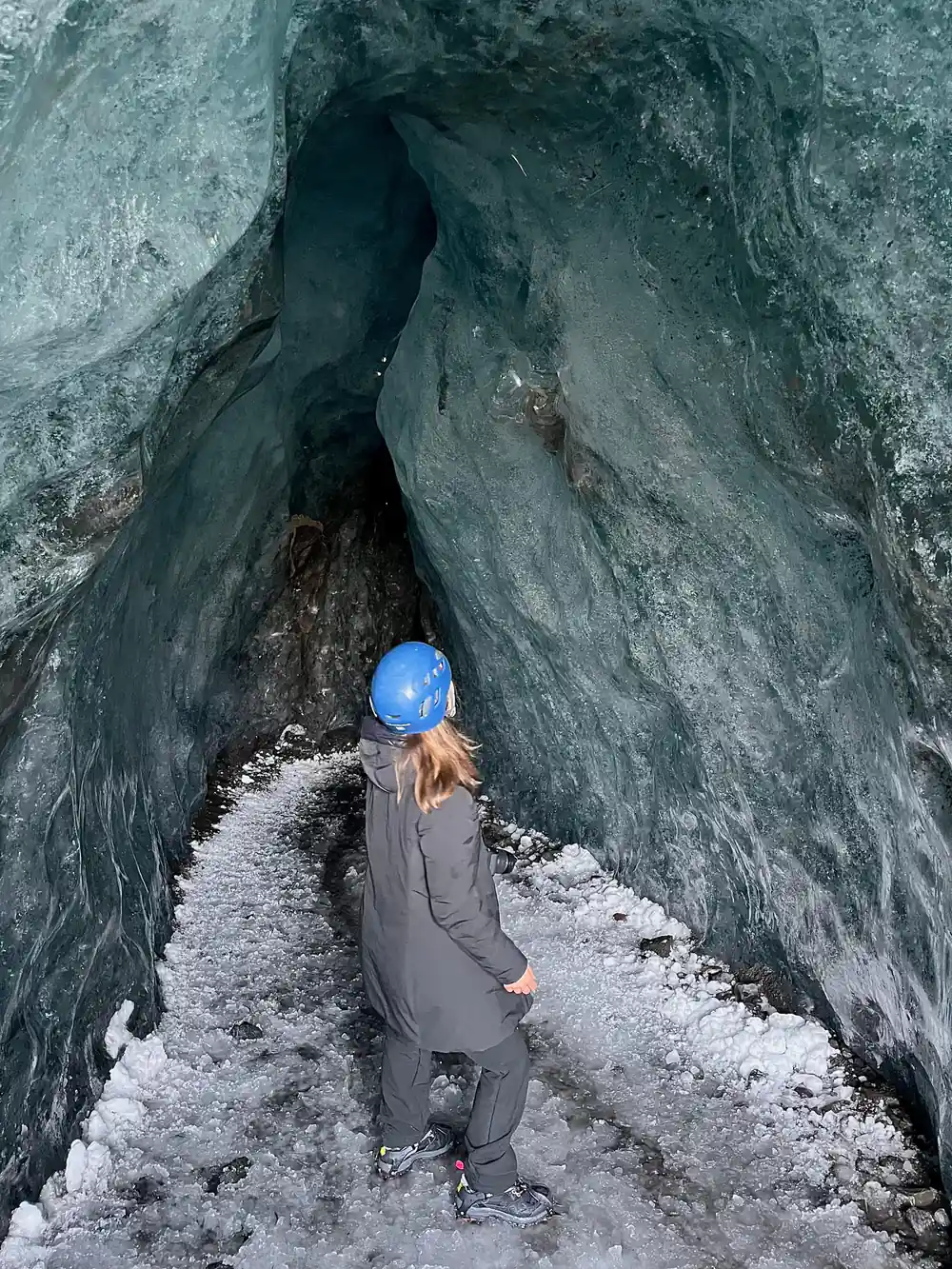 Person in blue hat walking in dark ice cavern
