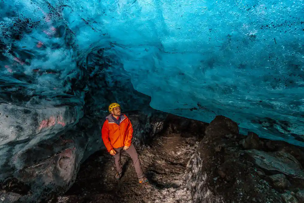 Person in orange jacket inside blue ice cave