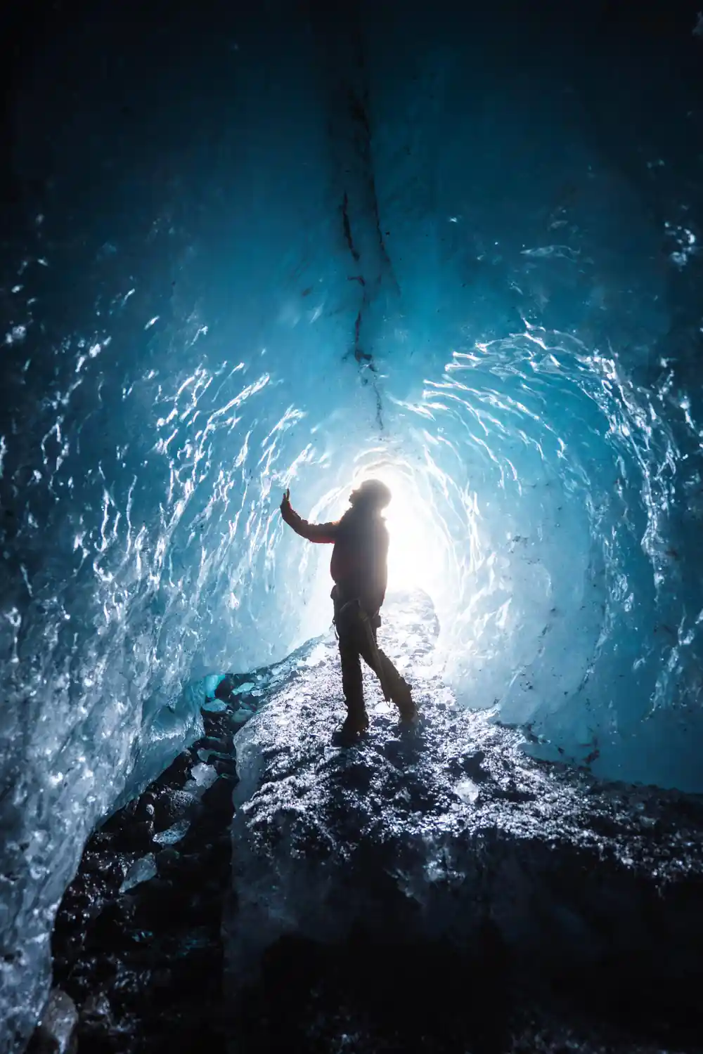 Person standing inside blue ice cave with light opening