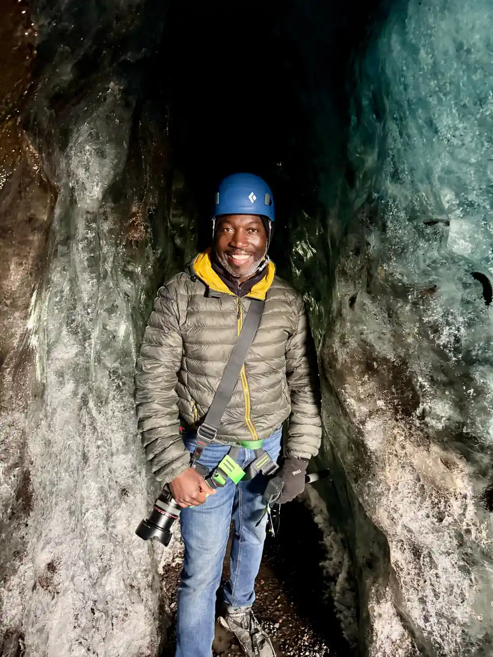 Person standing in narrow ice cave passage between blue walls
