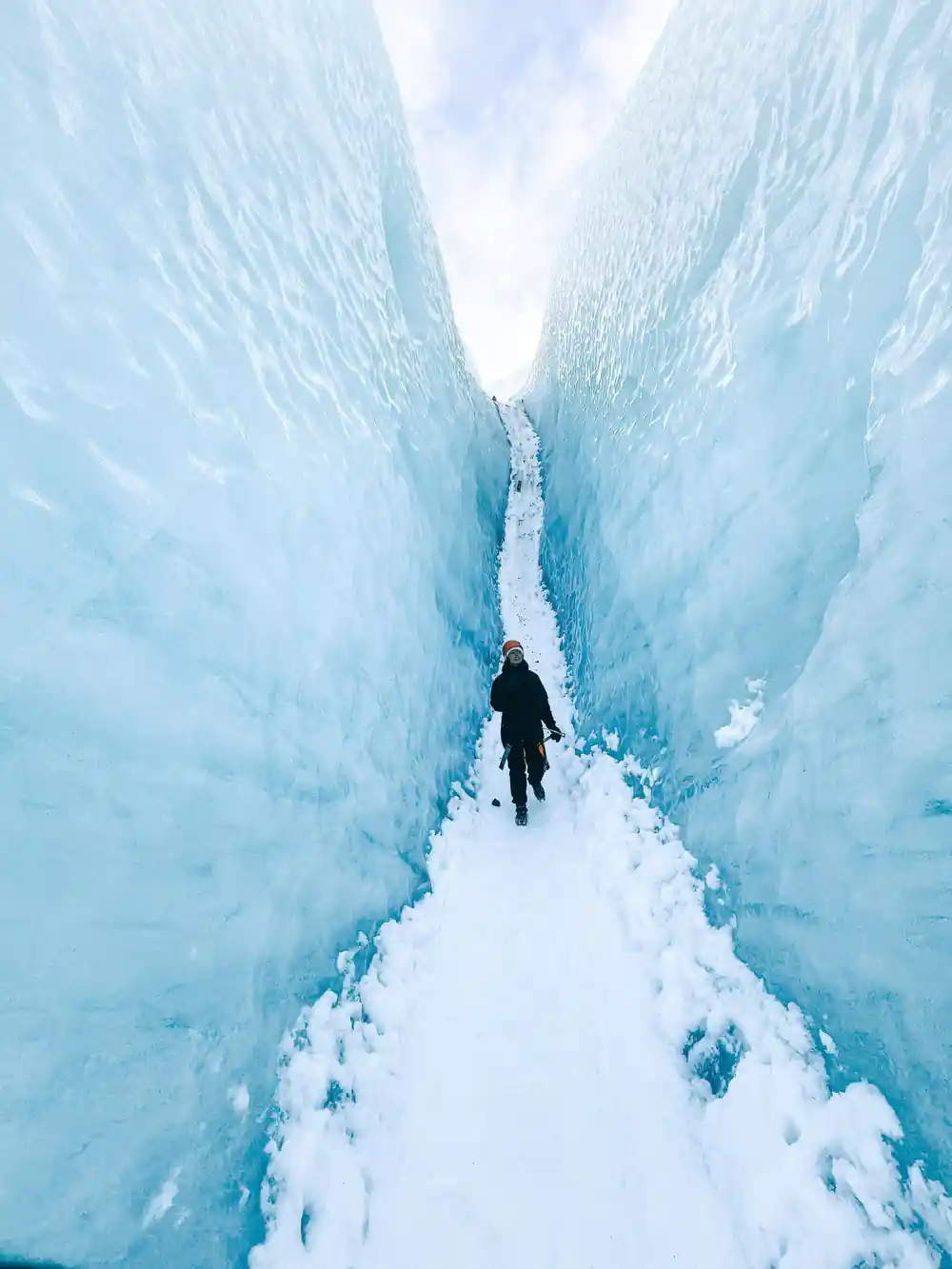 Person walking through narrow ice crevasse in glacier