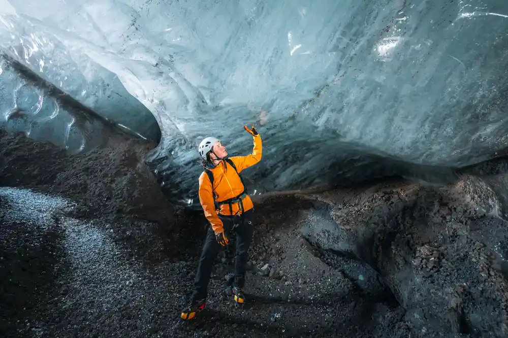 Person in yellow jacket under towering blue ice wall