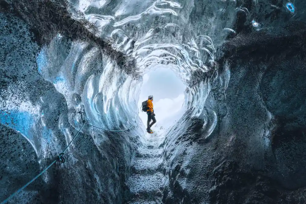 Solo hiker in yellow jacket in blue ice cave
