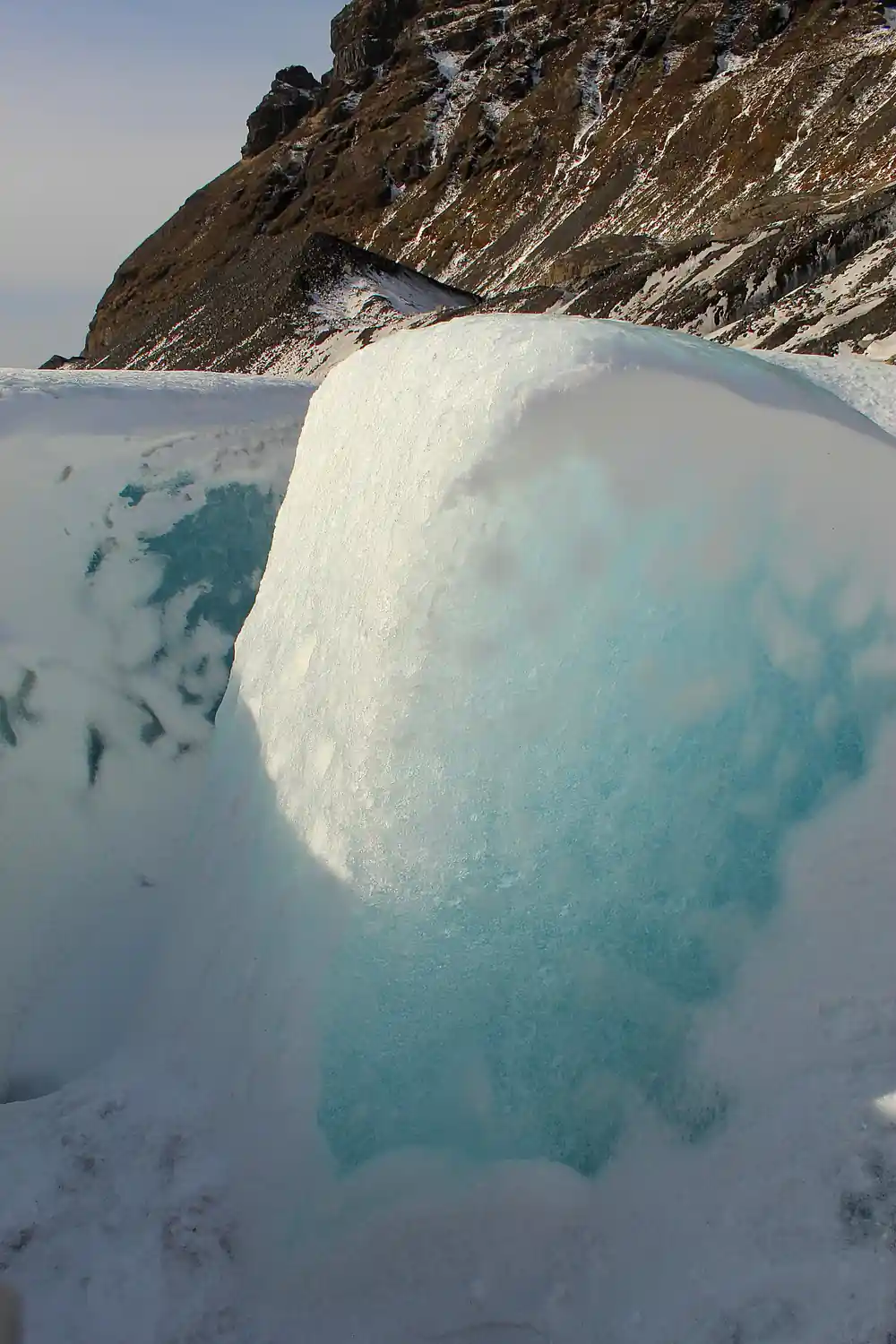 Turquoise ice formation on frozen lake near rocky cliff