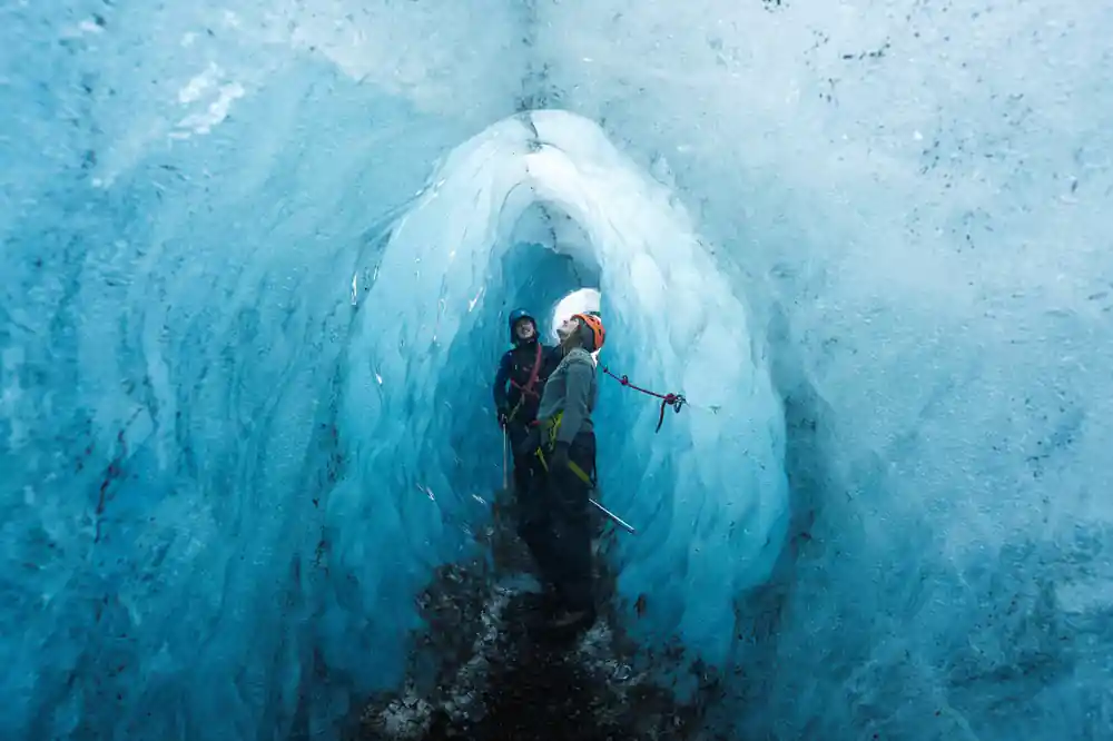 Two explorers inside large blue ice cave