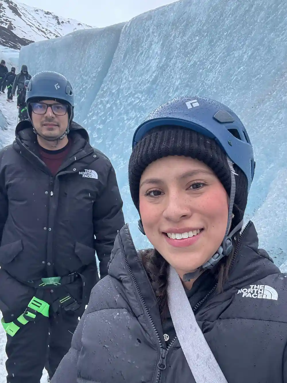 Two people in climbing gear on glacier with mountains behind