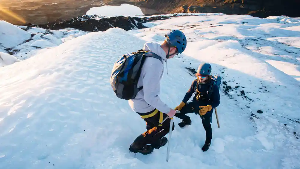 Two people on snow field near glacier cave opening