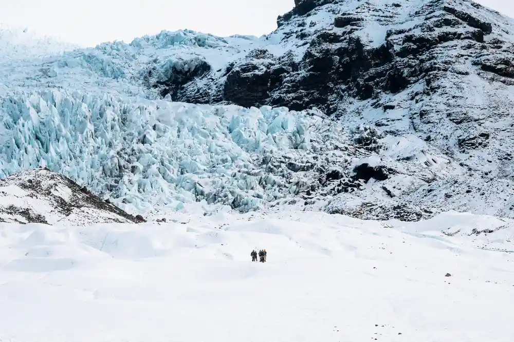 Two people on white snow field near glacier